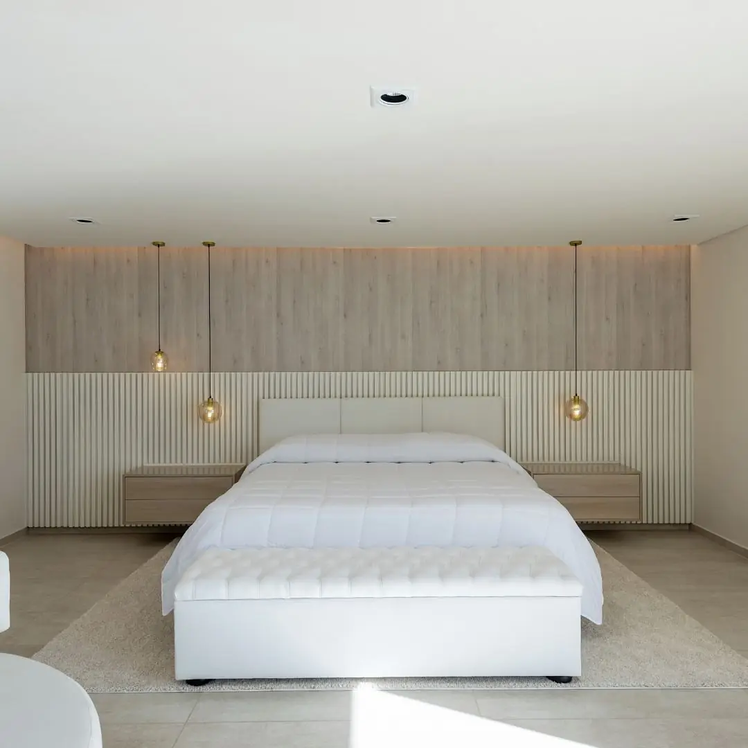 Dormitorio con respaldo panelado de madera y ranurado beige, mesas de luz flotantes y lámparas colgantes