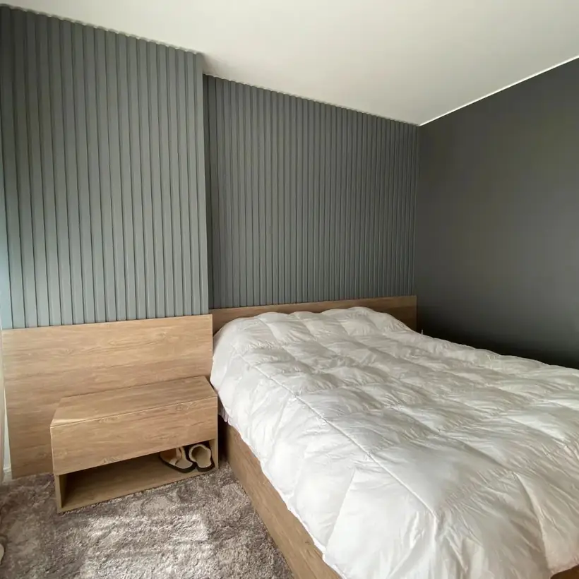Dormitorio con respaldo de madera, mesa de luz integrada y panel ranurado verde