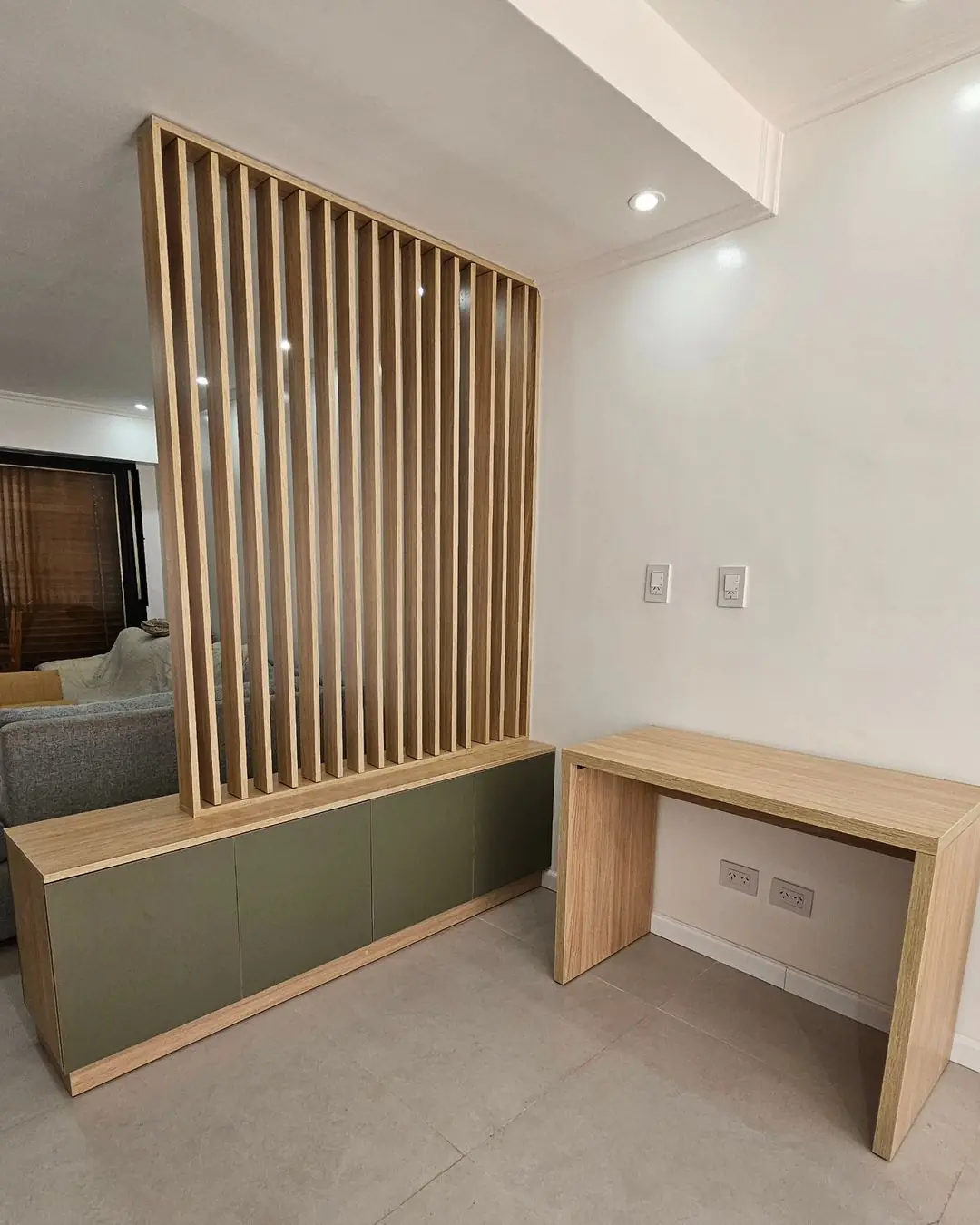 Divisor de listones de roble sobre un mueble bajo verde oliva, con escritorio al lado