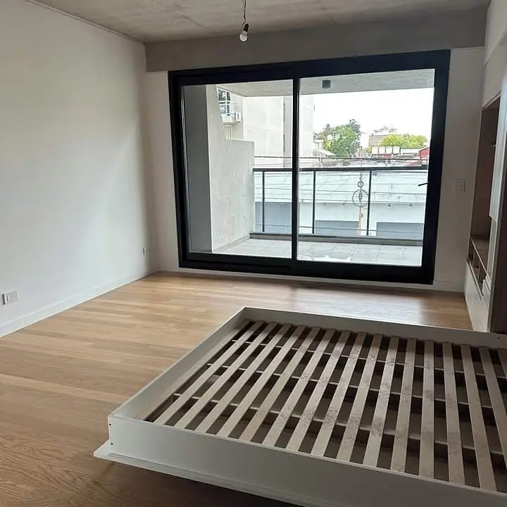 Cama rebatible abierta en un monoambiente, frente al ventanal