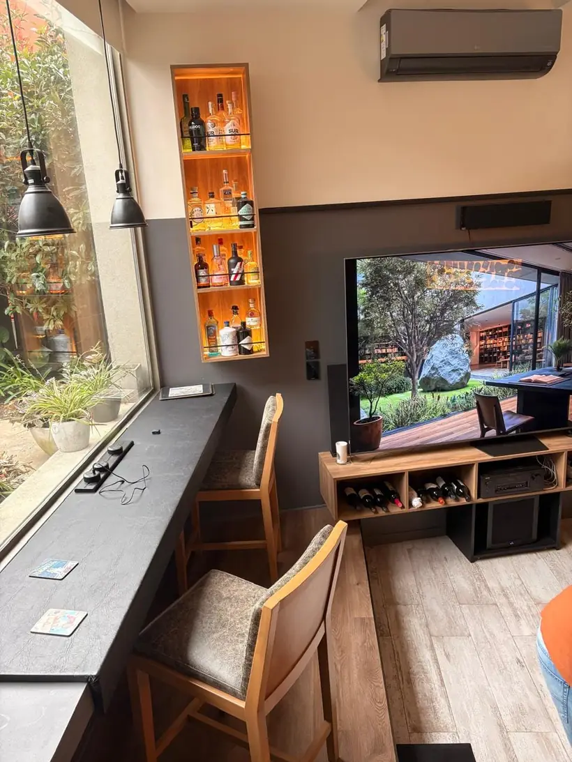 Barra bajo ventana con banquetas y rack de TV con botellero