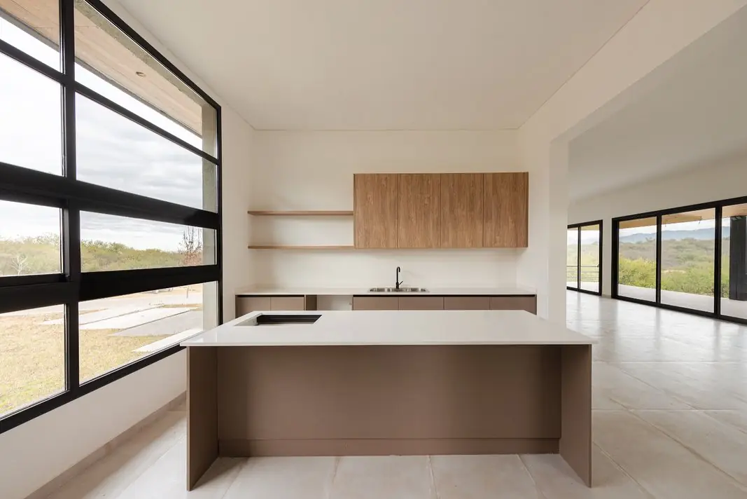 Cocina con isla central de mesada blanca y frentes en tono topo